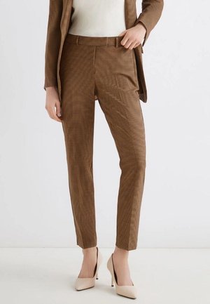 Pantaloni a quadri marroni realizzati in tessuto leggero, con vestibilità sartoriale, frontale piatto e pieghe sottili, abbinati a tacchi alti beige.