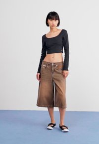 Brown denim wide-leg cropped pants with front pockets, a simple button closure, paired with a black long-sleeve fitted top and black flat shoes.