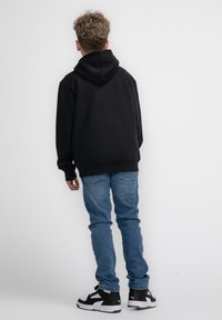 Felpa nera con cappuccio e maniche lunghe, abbinata a jeans azzurri e sneakers nere. Tessuto liscio con polsini e orlo a costine.