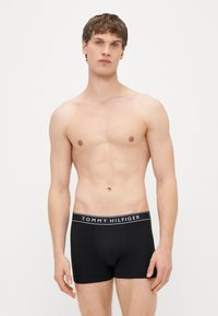 Cuecas boxers de algodão pretas com design ajustado, apresentando um cós elástico com a marca "TOMMY HILFIGER" em letras brancas.