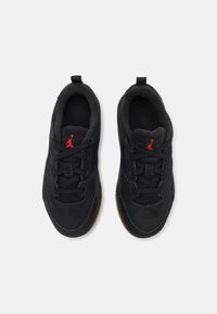 Des baskets en suède noir avec une finition texturée présentent des lacets noirs et un logo Jumpman rouge. La semelle a un accent en caoutchouc couleur caramel.