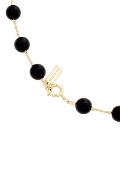 Collier en perles noires avec des perles rondes brillantes et des accents en métal doré, doté d'un fermoir de type homard et d'une étiquette attachée près du fermoir.