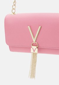 Bolsa de pele sintética cor-de-rosa com uma alça de corrente dourada, apresentando um proeminente logótipo em 'V' dourado e um detalhe de franja decorativa em corrente.