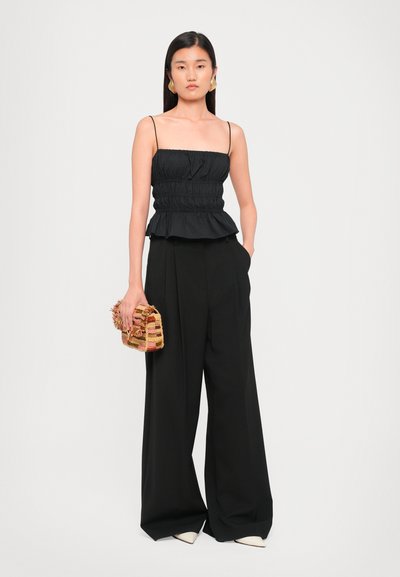 Black peplum top with adjustable spaghetti straps, paired with flowy black trousers and a textured multi-colored handbag.