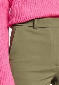 Pletený růžový svetr s ribbovanou texturou, ve spojení s hladkými, olivově zelenými kalhotami s jemným, přiléhavým střihem a bočními kapsami.