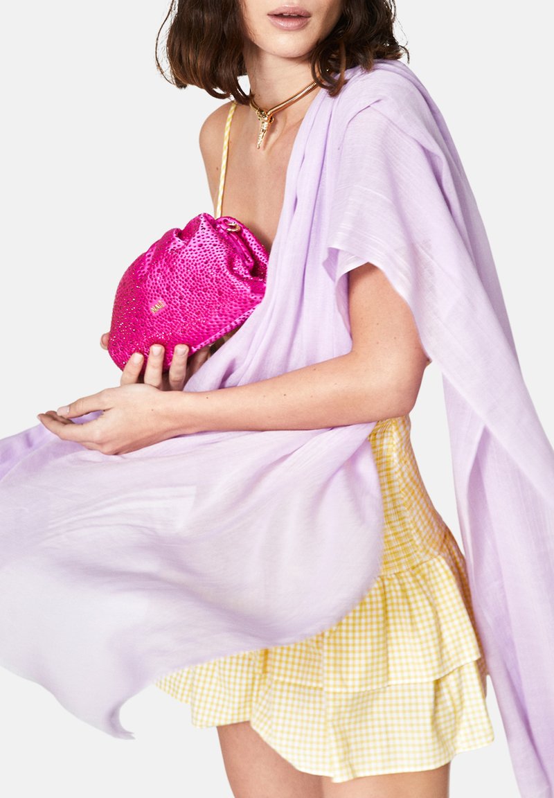 Borsa a sacco con paillettes fucsia e texture morbida, tenuta con una mano. Sciarpa trasparente lavanda sovrapposta a una mini gonna a quadretti gialli.