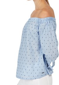 Top blu chiaro senza spalle con scollatura elastica, maniche lunghe e piccoli pois blu scuro. Presenta un dettaglio laterale con fiocco e un accento con logo.