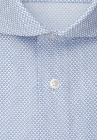 Camicia azzurra chiara con un piccolo motivo a triangolo blu scuro ripetuto e un singolo bottone bianco allacciato vicino al colletto.