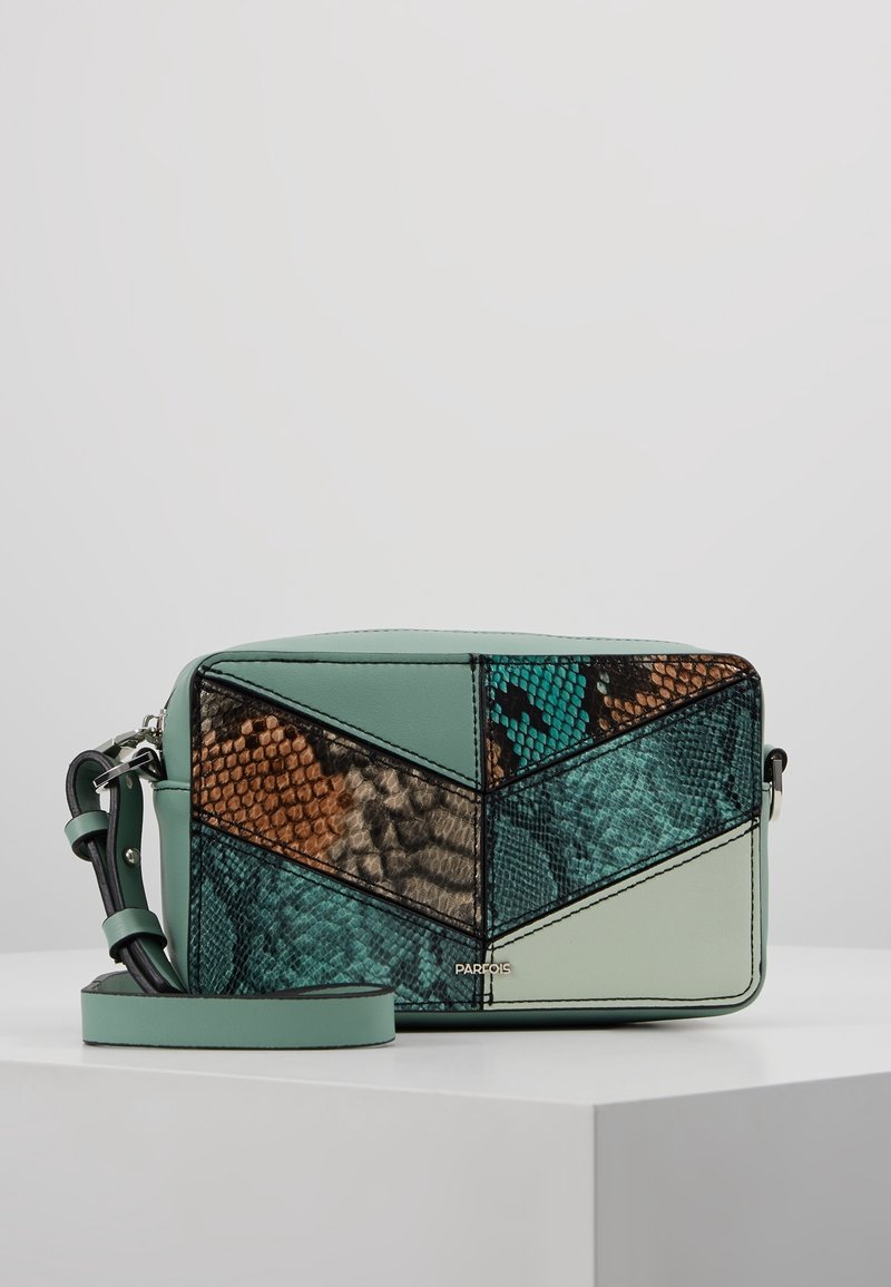 Piccola borsa a tracolla rettangolare con toppe geometriche multicolori in turchese, marrone e beige, con una tracolla removibile su una superficie bianca.