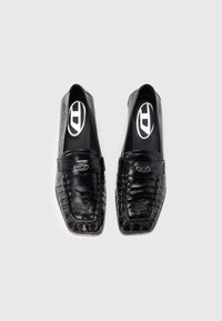 Mustad nahast mokassiinid, millel on läikiv viimistlus, ruudukujuline nina, tekstuuriga pind ning dekoratiivne rihm hõbedase pandlaga.