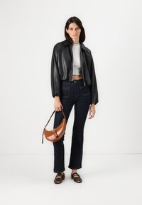 Giacca cropped in pelle nera, top bianco aderente, jeans svasati scuri, borsa in pelle coccodrillo marrone, e scarpe flat con stampa animale.