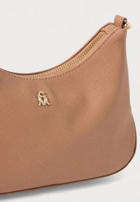 Tan textured handbag with gold zipper and hardware. Logo detail is visible on the front, showcasing a curved, minimalist design.