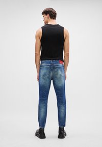 Falmede blå denimjeans med rett passform, baklommer og et rødt merke synlig ved midjen, sammen med en svart ermeløs topp.