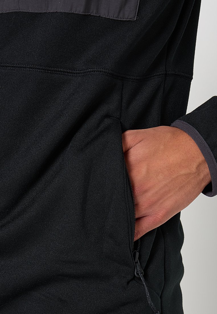Pull noir avec un design à demi-zip, doté d'une poche avant et d'accents gris contrastants aux poignets. Texture de tissu lisse et extensible.