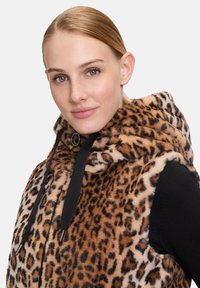 Kamizelka w panterkę z kapturem, z czarnymi sznurkami i miękką, puszystą teksturą. Projekt zawiera wysoki kołnierz i boczne kieszenie.