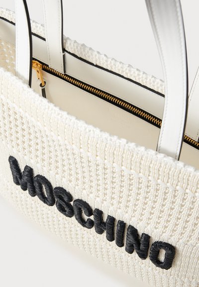 Sac à main tissé blanc avec broderie noire "Moschino", poignées en cuir blanc et une fermeture éclair dorée visible à l'intérieur.