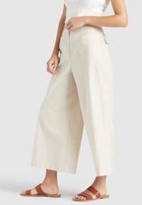 Beige wijde broek met hoge taille, gemaakt van een lichtgewicht stof, met achterzakken en een relaxte pasvorm, gecombineerd met een paar bruine sandalen.
