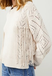 Maglione a maglia crema con motivi geometrici, dettagli testurizzati e accenti con frange lungo le maniche. Materiale morbido e leggero.