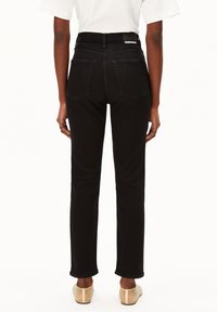 Un jean noir taille haute avec une coupe droite, deux poches arrière et une étiquette de marque au niveau de la taille. Texture en denim lisse.
