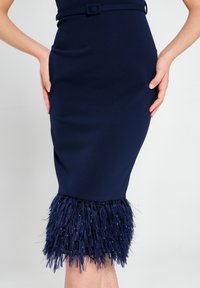 Marineblauer Bleistiftrock mit tailliertem Schnitt, der am Saum mit einer strukturierten, federartigen Fransenverzierung und einem passenden Gürtel in der Taille versehen ist.