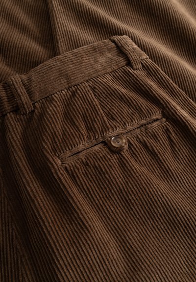 Close-up of brown corduroy fabric trousers with a buttoned back pocket and belt loops.