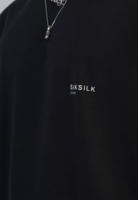 Fekete, rövid ujjú, pamut póló sima textúrával, a mellkason a fehér "SIKSILK" márkájú logóval és az "Est 2012" felirattal. 