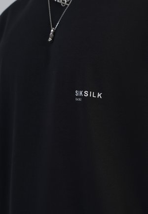 Črna majica s kratkimi rokavi iz bombaža z gladko teksturo, ki na prsih prikazuje belo blagovno znamko "SIKSILK" in "Est 2012".