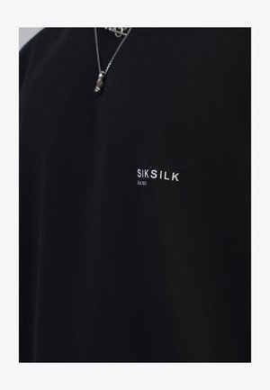 Camiseta negra de mangas cortas hecha de algodón con una textura suave, que presenta el logotipo blanco de la marca "SIKSILK" y "Est 2012" impreso en el pecho.