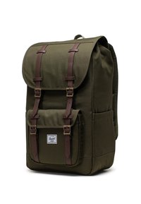 Zaino verde oliva con una parte superiore pieghevole, cinghie in pelle e fibbie in metallo. Presenta una tasca frontale e un'etichetta con il marchio sul lato.