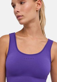 Fioletowy sportowy top na ramiączkach wykonany z gładkiej, elastycznej tkaniny. Posiada dekolt w kształcie litery U i subtelne czarne logo.