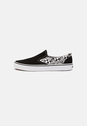 Chaussure Vans slip-on noire et blanche avec motif damier et texte au talon et sur le côté, semelle en caoutchouc blanche et couture blanche.