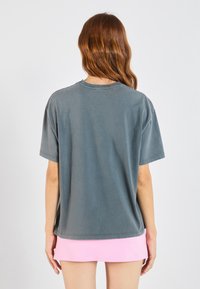 Pilkas medvilnės marškinėlis trumpomis rankovėmis, pasižymintis laisvu siluetu ir apvaliu kaklu. Hemas šiek tiek krenta žemiau liemens.