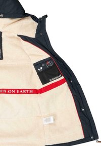 Granatowa kurtka z beżową podszewką z polaru, czerwoną opaską z napisem "KOBIETY NA ZIEMI", oraz wieloma wewnętrznymi kieszeniami na akcesoria.