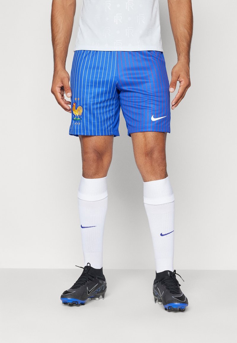 Blå fotbollsshorts med vertikala ränder och broderad tupp, tillsammans med vita strumpor och svarta fotbollsskor med blå detaljer. Nike-logotypen är närvarande.