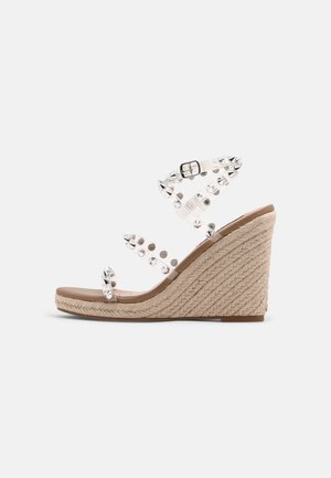 Beige kile-sandal med flettet reb-hæl og klare stropper dekoreret med sølvnitter og lukning med spænde.