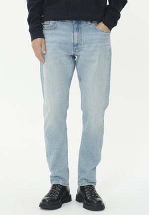 Világoskék farmernadrág, egyenes szárú dizájn, öt zsebes stílus, fekete fűzős bakancsokkal párosítva, sima textúra, minimális kopás.