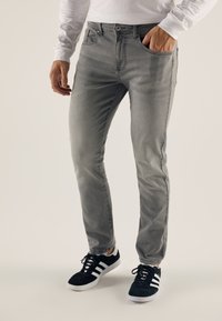 Jean gris avec une coupe slim, design classique à cinq poches et légères décolorations. Associé à des baskets noires avec des accents blancs.