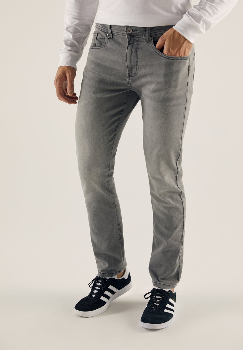 Jean gris avec une coupe slim, design classique à cinq poches et légères décolorations. Associé à des baskets noires avec des accents blancs.
