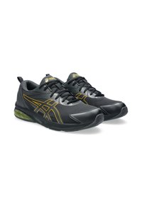 Zapatillas deportivas negras con parte superior de malla, acentos plateados y amarillos, punta redondeada y suela acolchada verde. Incluye cordones y una lengüeta.