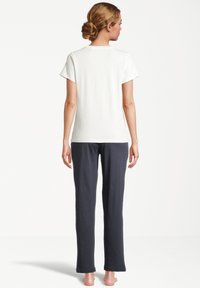 Vit t-shirt i bomull med korta ärmar som bärs tillsammans med mörkblå byxor. Enkelt design, avslappnad passform och mjuk textur. Inga mönster eller detaljer.