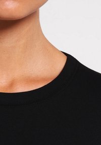 Svart bomulls t-shirt med ribbad rund halsringning, slät textur och figurnära design. Tyget verkar lätt och andas.