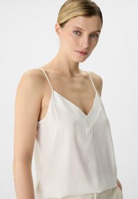 White silk camisole with thin straps, featuring a deep V-neckline and a smooth, lightweight texture. Elegant and minimalist design.