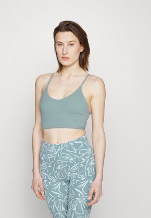 Top desportivo verde claro com decote em V e alças finas, combinado com leggings estampadas apresentando desenhos florais brancos sobre um fundo correspondente.