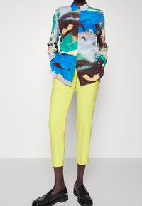 Färgglad, abstrakt mönstrad siden skjorta med knäppning vid kragen, kombinerad med slim fit, klara gula byxor och svarta loafers.