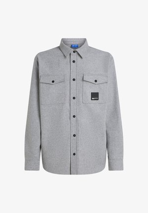 Camisa de franela gris de manga larga, con botones en la parte delantera, dos bolsillos en el pecho y un parche de logo negro. Presenta botones negros y un cuello clásico.