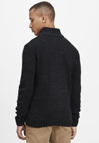 Svart tröja med hög krage, strukturerad stickning och färgglada prickar genom hela. Ribbad ärm och fåll, figurnära silhuett, ingen synlig branding.