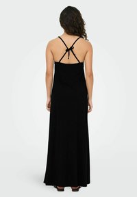 Robe maxi noire en tissu doux et fluide. Elle comporte des bretelles spaghetti ajustables et un détail noué au dos. Design simple et sans couture.