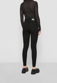 Leggings noirs taille haute en matière extensible. Dotés d'une étiquette à la ceinture arrière, de deux poches arrière et d'une coupe ajustée.
