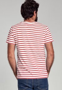 Witte t-shirt met horizontale rode strepen, korte mouwen en een ronde halslijn, gecombineerd met blauwe denim jeans.