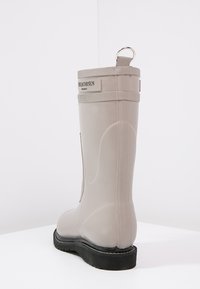 Botte de pluie en caoutchouc beige avec des panneaux latéraux texturés et une semelle noire robuste. Dispose d'une languette arrière pour un enfilage facile.